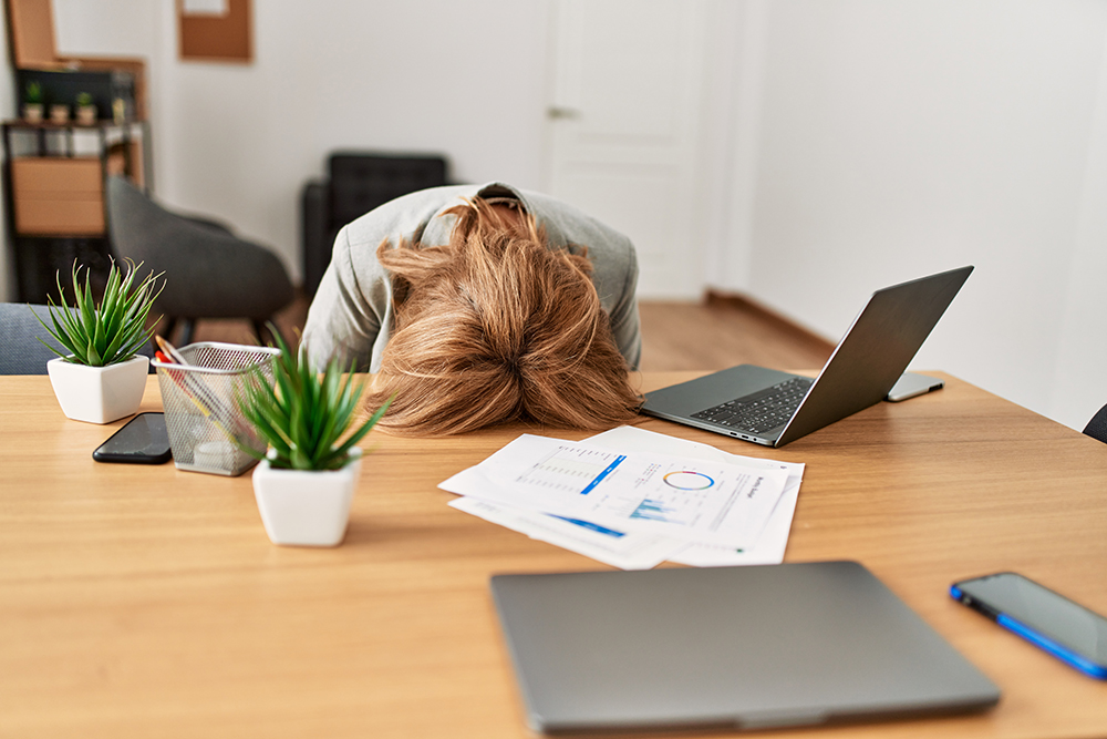 Middle age businesswoman overworked with head on desk at the office. Photo of a woman leaning her head on a desk in an office, looking exhausted.