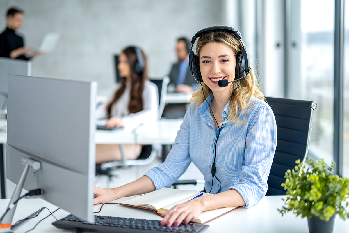 Portrait of female operator ready for online assistance at call A woman in a light blue shirt wearing a headset in a call center.