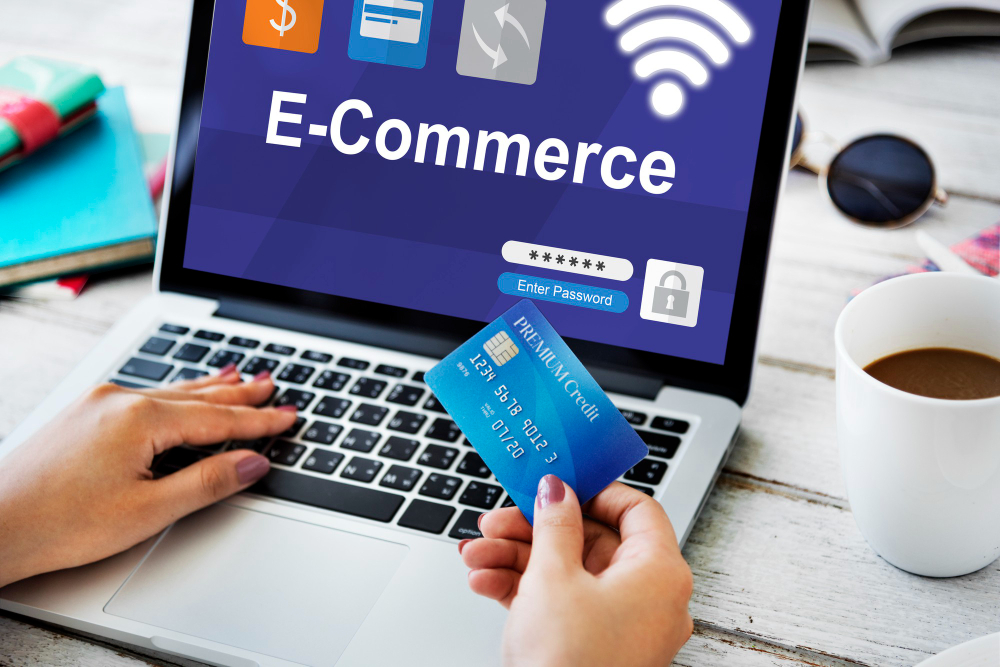 A laptop showing "E-Commerce" with a person using a credit card for a secure transaction.