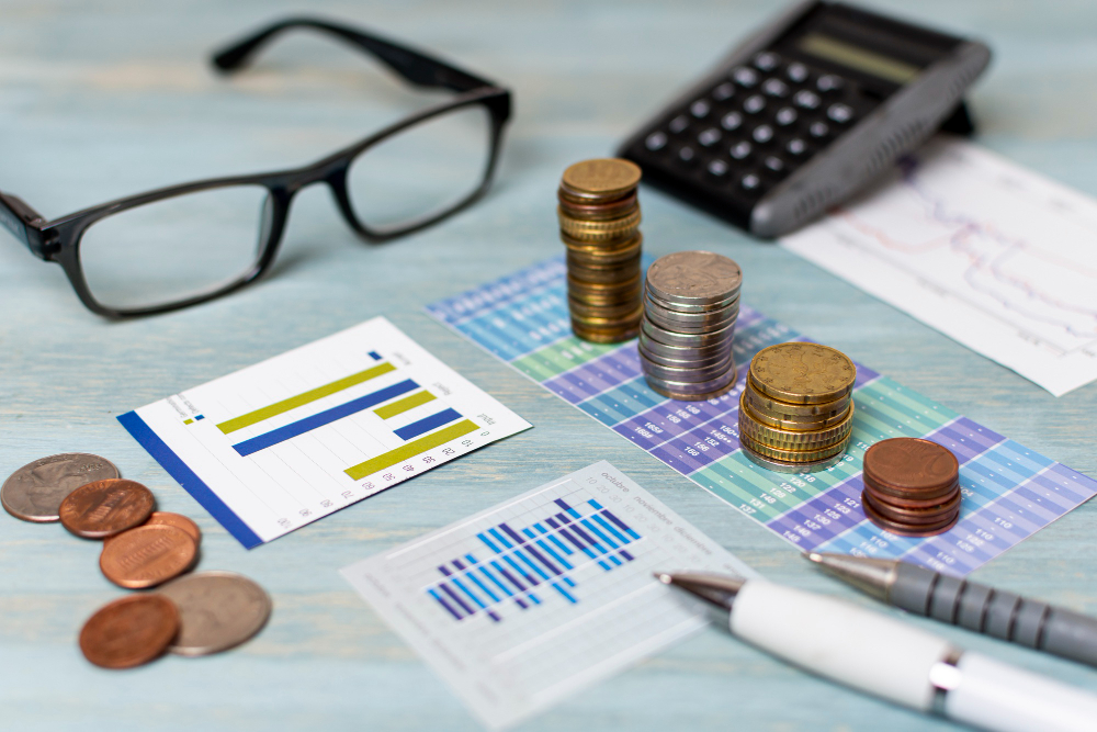 Close-up of coins, a calculator, and financial charts on a desk.
