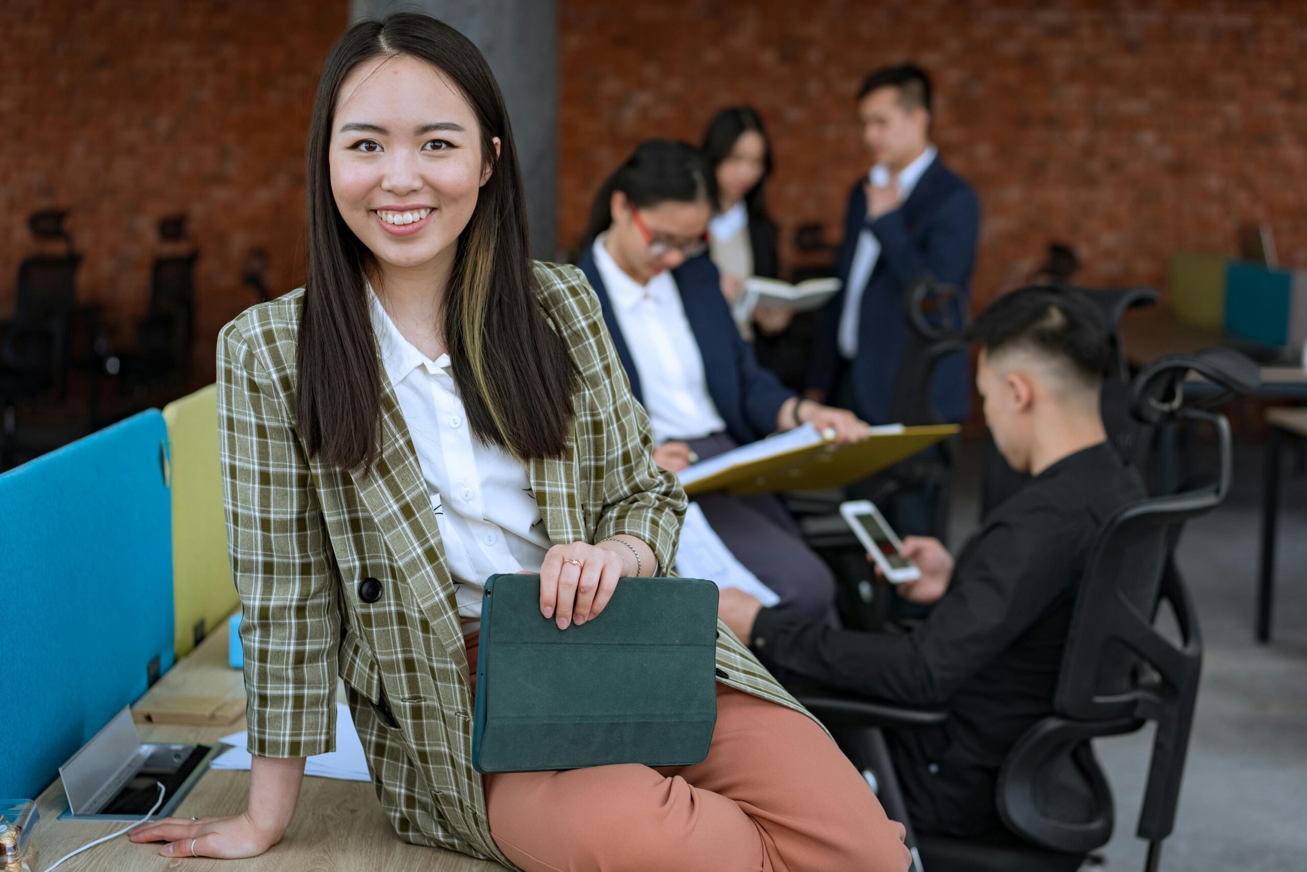 A professional Altselino virtual assistant smiling while holding a tablet in a modern, collaborative office setting.